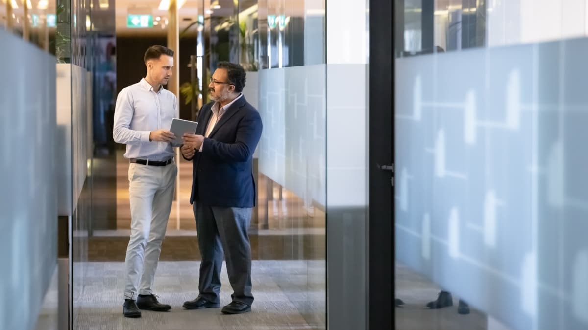 Discussion entre un employé et son patron dans le couloir d'une entreprise.
